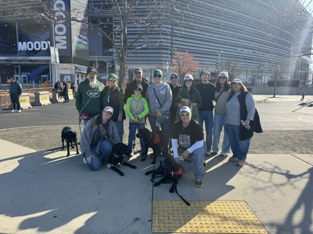 Group of people and dogs posing for a photo outside a stadium entrance with 'MOODY'S' signage visible.